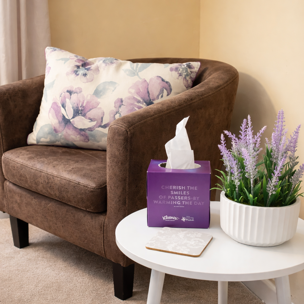 Brown armchair with light patterned cushion next to a small white table with a lavendar plant